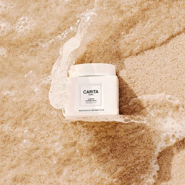A white Carita Baume Lagon jar sitting in the sand.