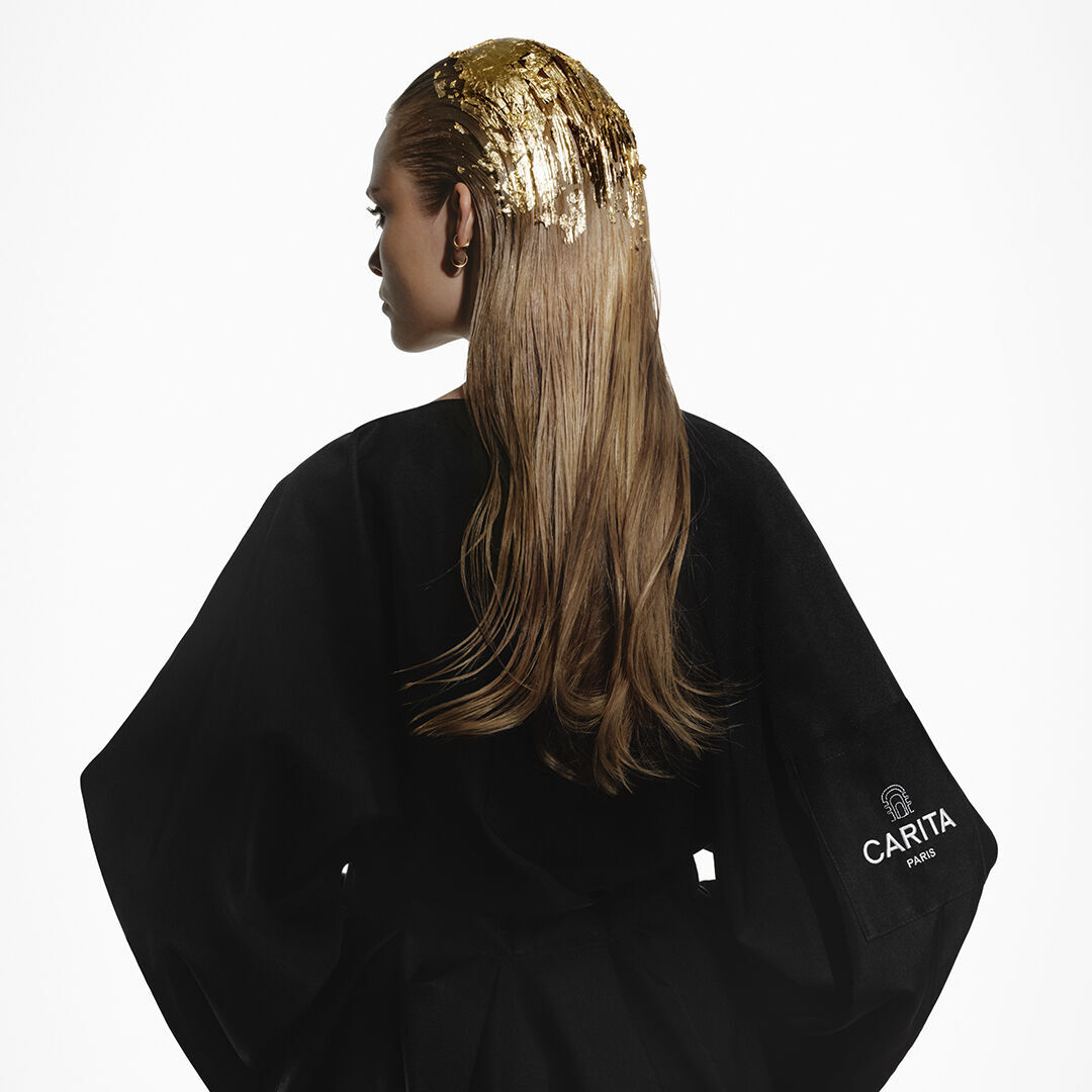 A blonde woman wearing a black Carita dressing gown, with gold leaves in her hair.