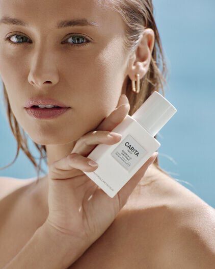 A close-up portrait of a woman holding the white Essence UV bottle.