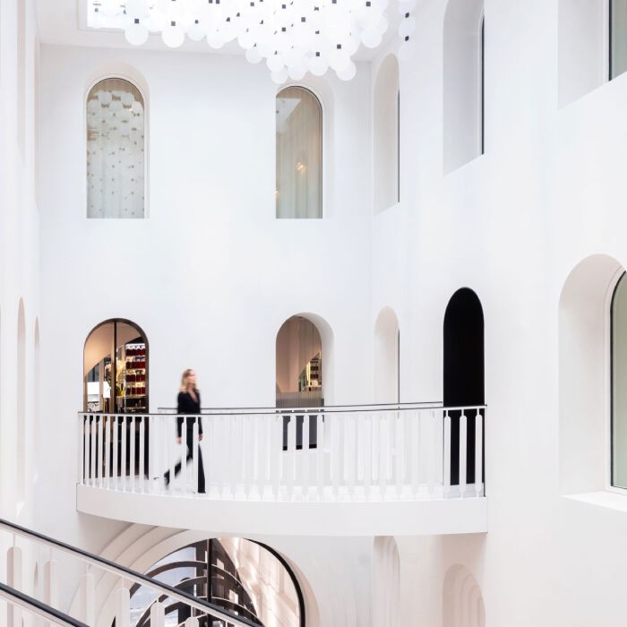 Carita Maison de Beaute: bright, modern interior with white walls, elegant arches, a curved balcony with a person walking, and a ceiling adorned with luminous circles.