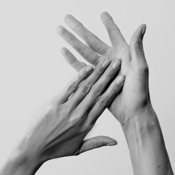 Monochrome close-up of hands in motion, one gently caressing the other, suggesting care or product application, with a neat manicure.