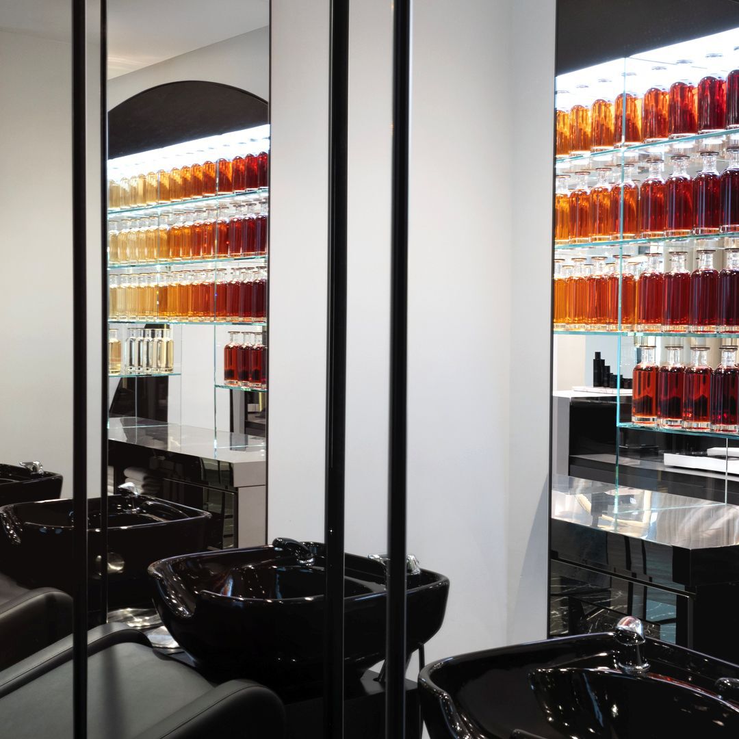 Modern and elegant hair salon featuring rows of product bottles, sleek black basins, and large mirrors, creating a sophisticated and clean setting.
