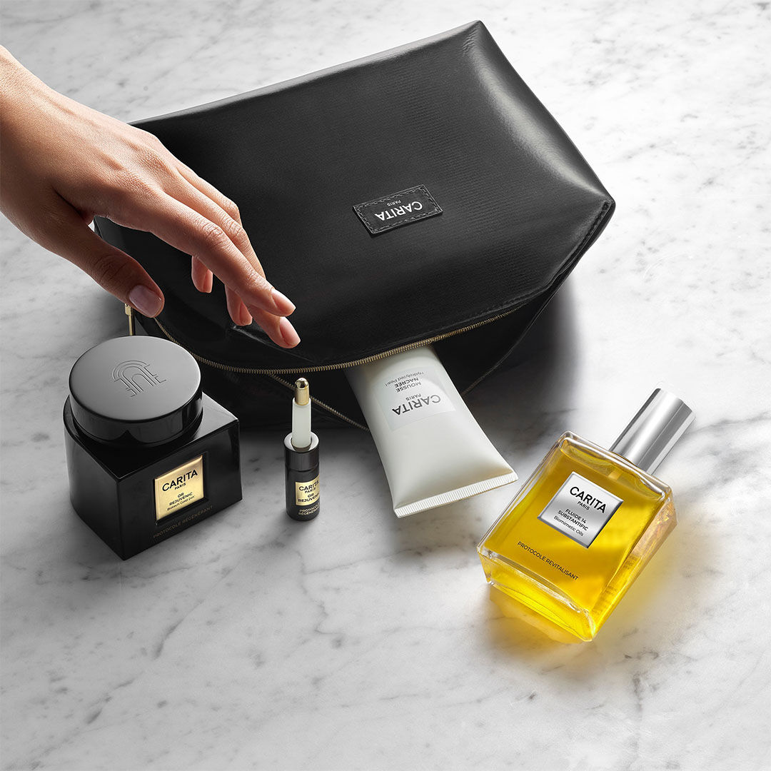 Carita beauty products and a black vanity bag on marble.​