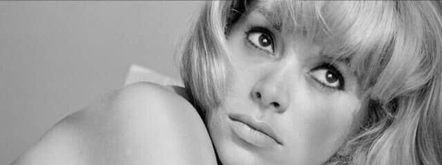 A close-up black-and-white portrait of a woman with short, wavy hair, gazing thoughtfully with a serious expression. Her face is partially turned, highlighting her features.