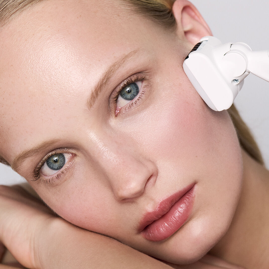 Woman receiving a facial treatment with a white device.