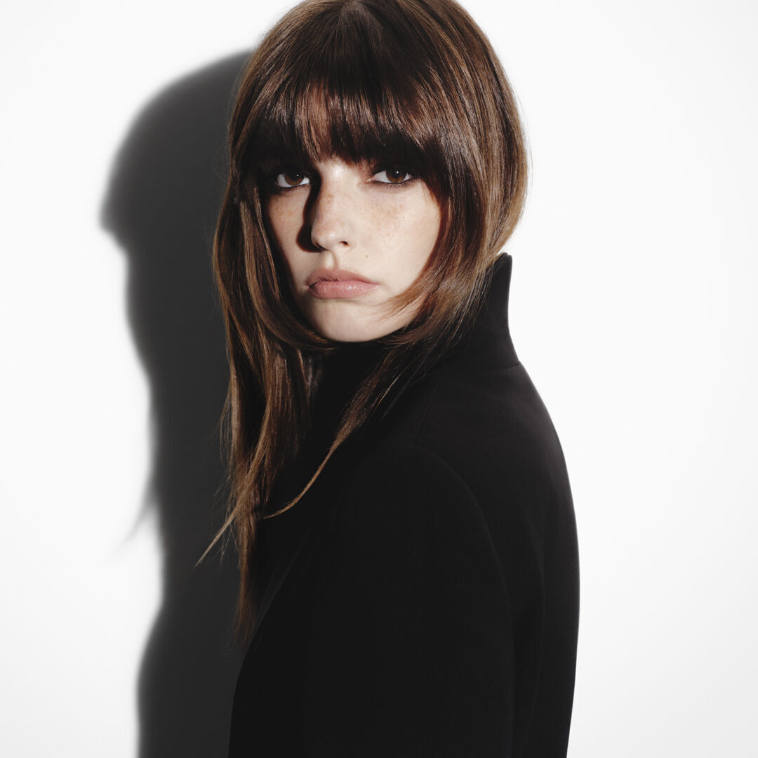 Brunette woman with bangs and a sleek Hair Rejuvenic blowout.