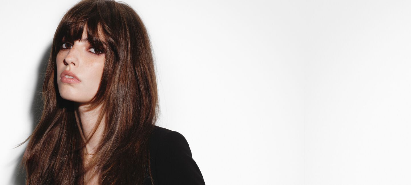 A brunette woman with fringe and a silky Hair Rejuvenic blow-dry.