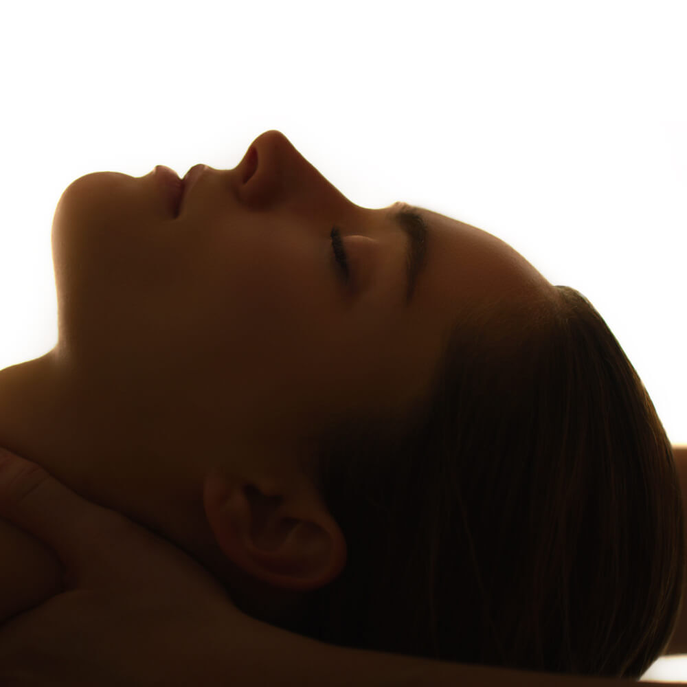 A close-up profile of a person with their eyes closed and head tilted back, illuminated against a bright, diffuse background. The focus is on their serene expressions and smooth features.