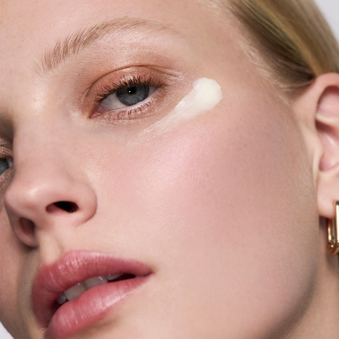 Applying a dab of cream to a woman’s cheekbone.