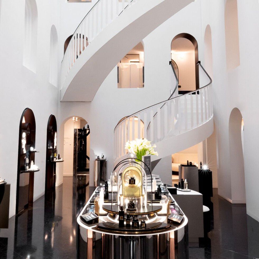 Carita Maison de Beaute: modern interior with a white spiral staircase, arched walls, and glossy black floor, showcasing beauty product displays.