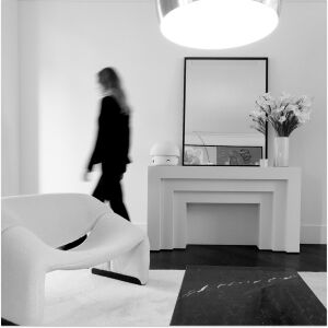 Monochrome modern interior with a blurred person walking, an elegant console table, mirror, flowers, and a white designer armchair. 