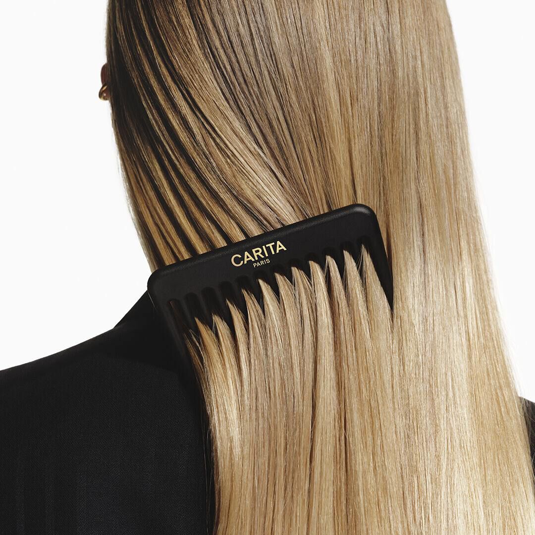 A black Carita comb detangling long, straight blonde hair.
