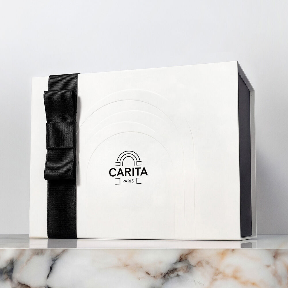 A white Carita Paris luxury gift box with an elegant black ribbon bow, presented on a marble surface.