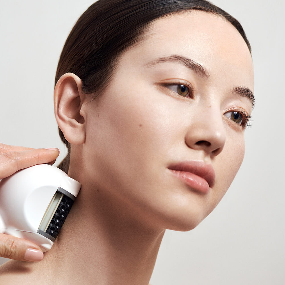 Woman receiving anti-aging icoone treatment for drained, lifted, firm skin (left), with the icoone device (right). Elegant design on light background.