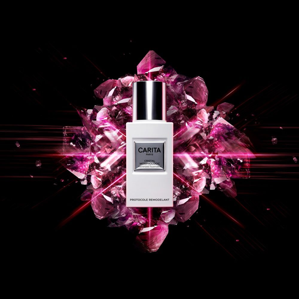 A sleek white bottle of Carita skincare product is centered against a dramatic black background, surrounded by vibrant pink gemstones and sparkling effects, highlighting the luxurious nature of the product.