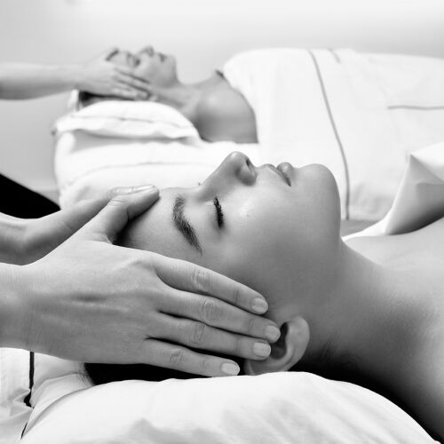 Two individuals receive relaxing facial massages in a serene spa setting, captured in black and white, highlighting tranquility and shared well-being.