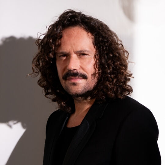 Portrait of a man looking direct, with prominent mustache and thick, curly hair.