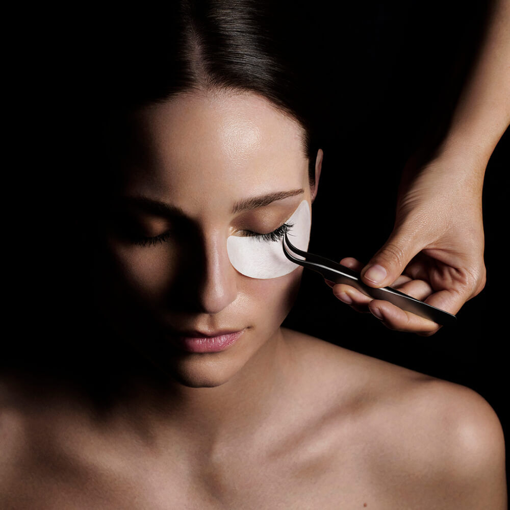 Dramatic eyelash application with tweezers in focused light.