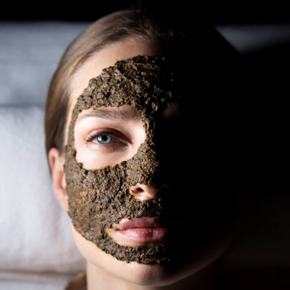 Close-up of a woman wearing a dark, textured exfoliating face mask.