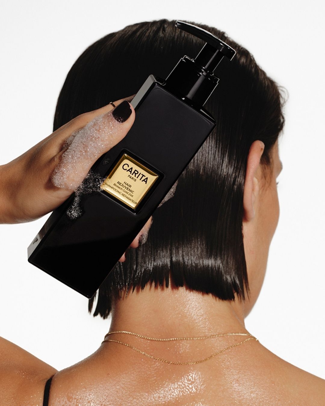 A woman with short hair holding Carita Repairing Shampoo.