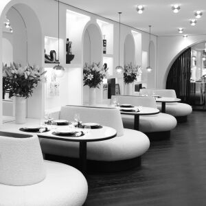 Elegant and modern restaurant interior with curved booth seating, set round tables, and decorative arches with flowers.