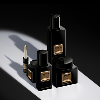 A collection of elegant black skincare bottles and jars with gold labels, arranged on a dark surface with dramatic lighting and shadows.