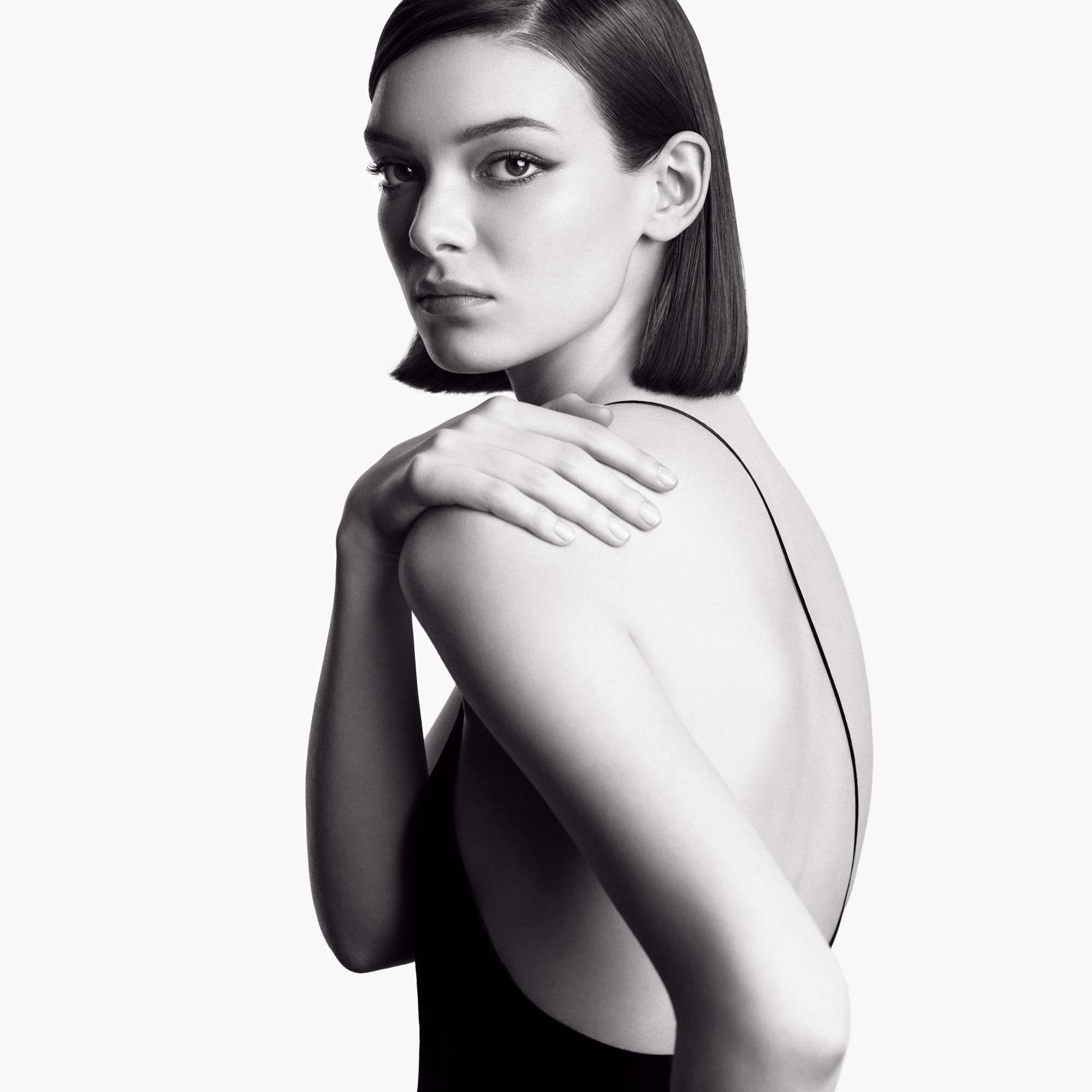 Monochrome portrait of a short-haired woman, posing with her back to the camera and looking over her shoulder, with an intense, sophisticated expression.