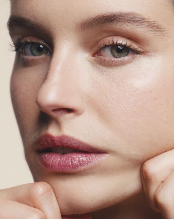 A close-up portrait of a woman applying skincare to her cheeks.