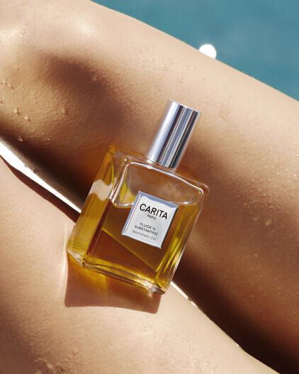 A bottle of Fluide 14 golden oil resting on satiny skin.