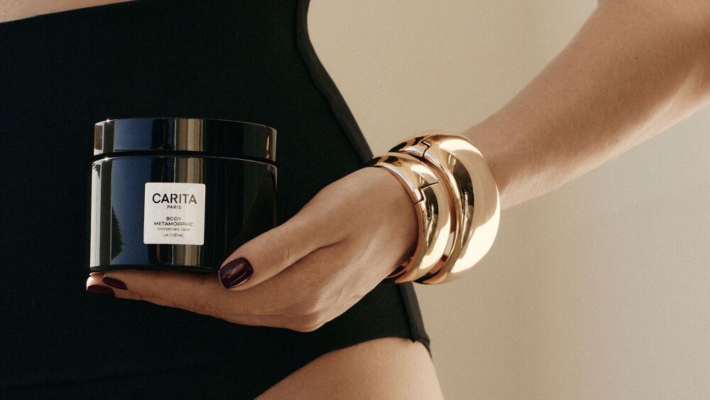A woman in a swimsuit holding the Body Metamorphic jar.