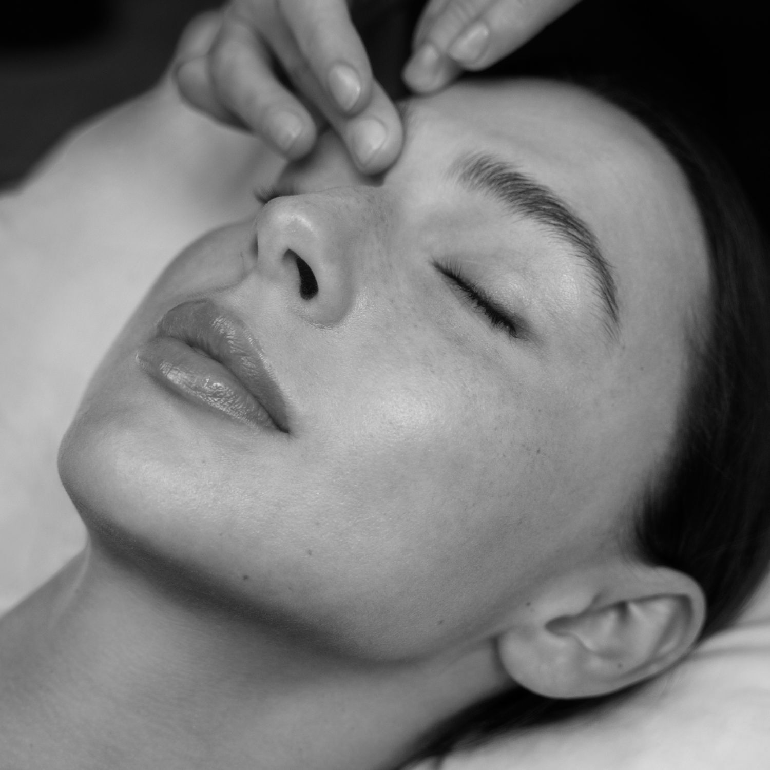 Monochrome close-up of a relaxed woman receiving a forehead massage with closed eyes, conveying a sense of care and well-being.