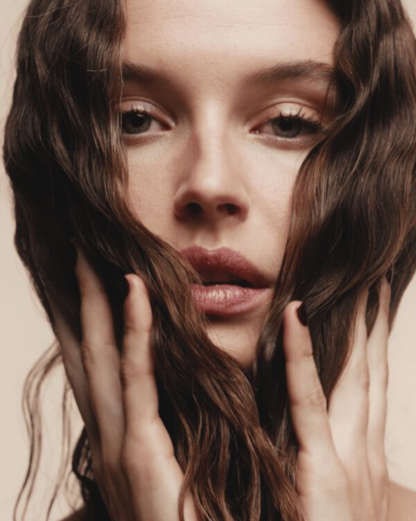 A brunette woman seen in profile, touching her hair.