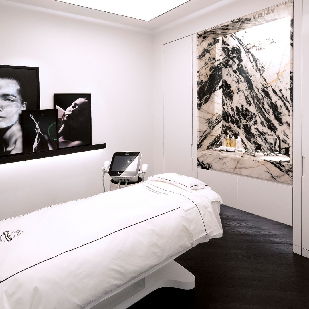 Modern, luxurious treatment room with a pristine bed, advanced beauty equipment, and a striking black and white marble wall. Elegant space.