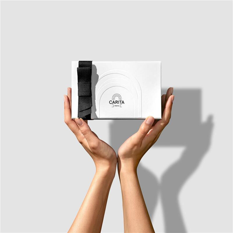 A woman's hands holding a white Carita Paris luxury gift box featuring an elegant black ribbon bow.