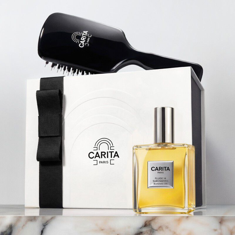 Carita Paris gift set featuring a black hairbrush, the iconic Fluide 14 oil, and a white gift box with a black ribbon.
