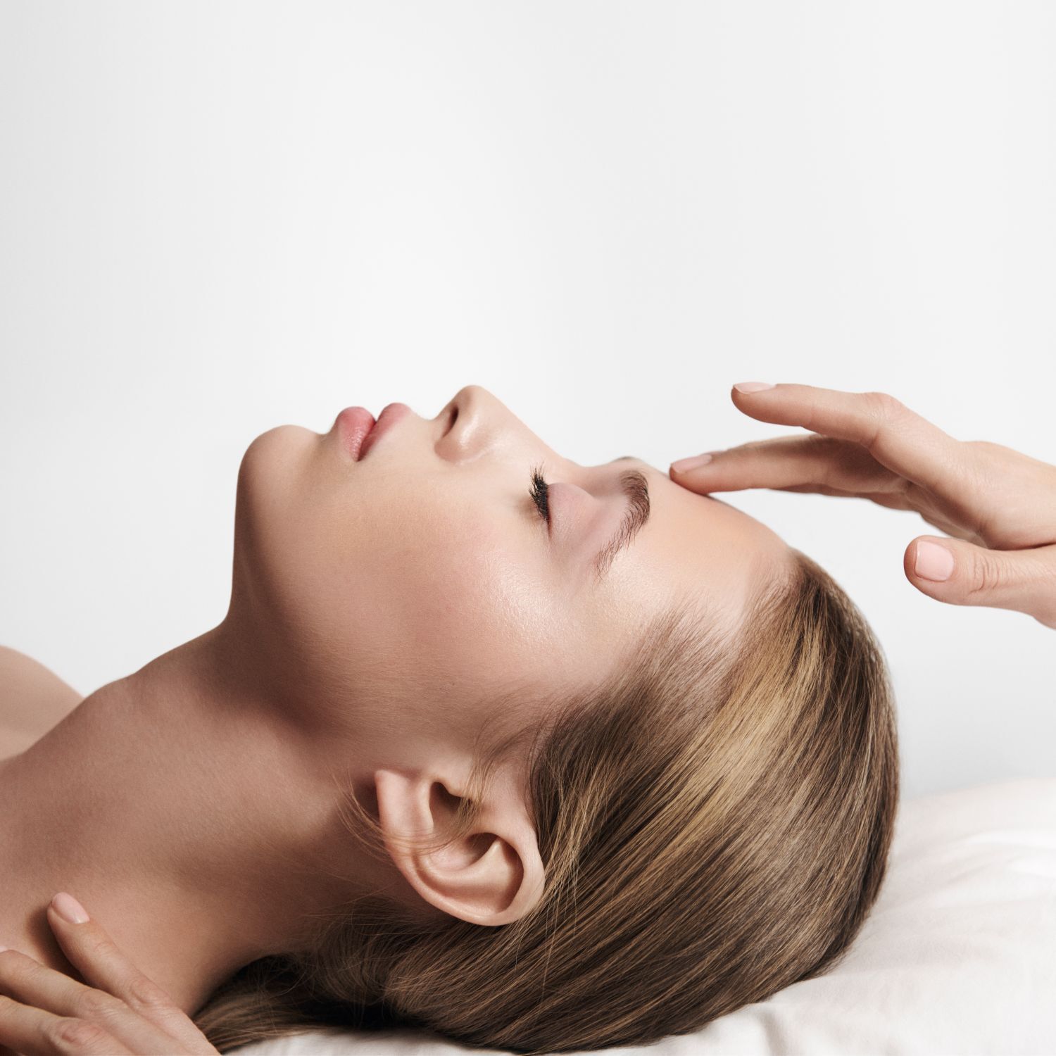 A relaxed woman receives a facial treatment, a hand gently caressing her forehead, symbolizing serenity and well-being.